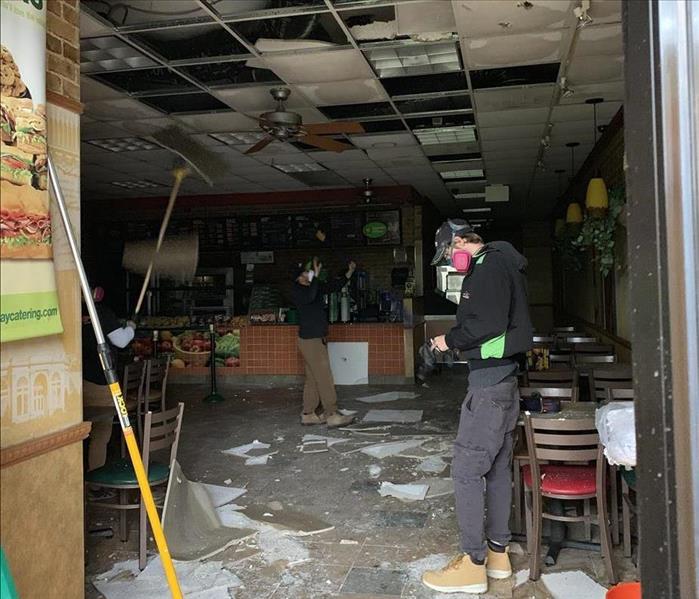 three SERVPRO workers inside fire damaged restaurant with cleaning tools 