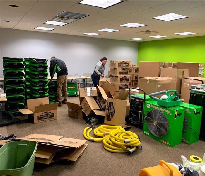 two SERVPRO employees unboxing drying fans and restoration equipment in a large storage room  